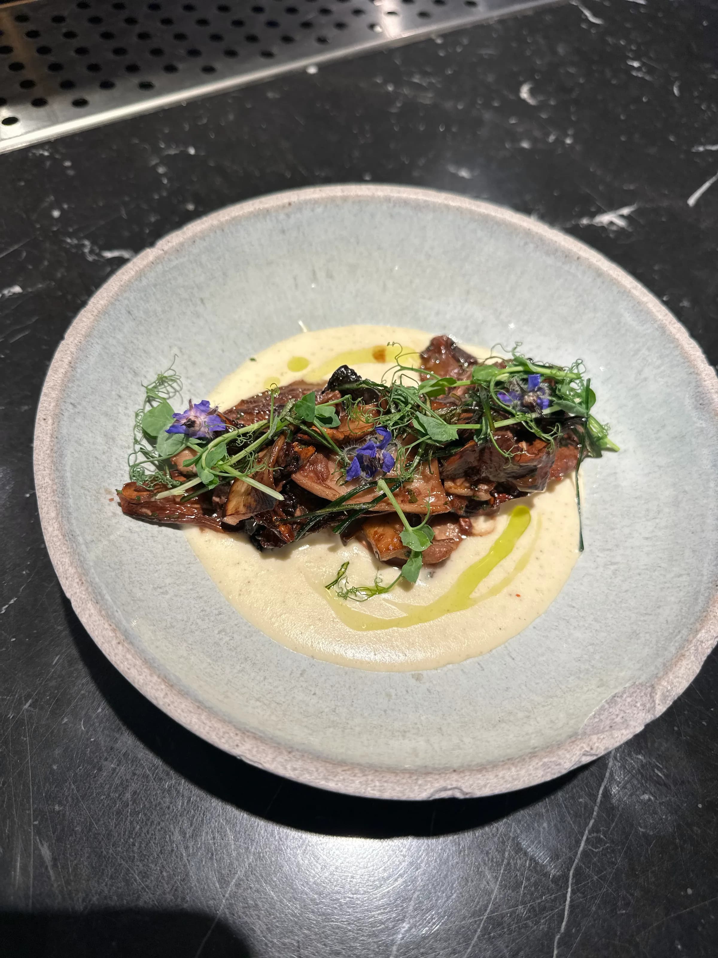 Mushrooms over a creamy puree with pea shoots and edible flowers